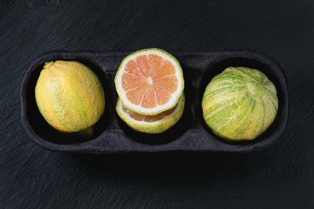 whole and sliced citrus fruit pink tiger lemon in paper market box over black stone slate textured background. Top view with space. Modern healthy eatingの写真素材