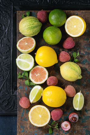 Variety of whole and sliced citrus fruits pink tiger lemon, lemon, lime, mint and exotic lichee over dark ornate and old wooden background. Top view. Healthy eatingの写真素材