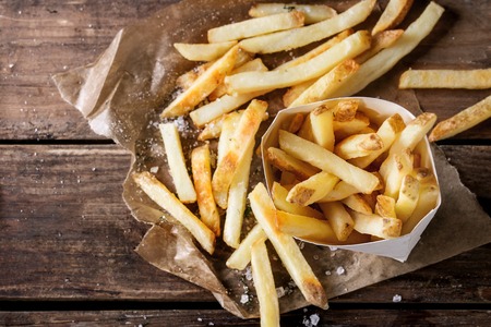 Fast food french fries potatoes with skin served with salt and herbs in lunch box on baking paper over old dark wooden background. Top view, space for textの写真素材