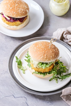 Two vegetarian hamburgers with onion and cheese cutlets, avocado salad, arugula, fried beetroot and yogurt sauce in white plate over gray texture background. Healthy fast food.の写真素材