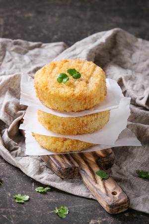 Stack of Cheese and onion veggie cutlets for making vegan burger, served on wooden board with herbs, paper and textile on dark background. Healthy vegan diet meal.の写真素材