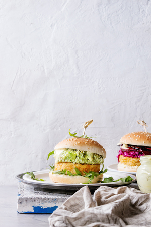 Two vegetarian hamburgers with onion and cheese cutlets, avocado salad, arugula, fried beetroot and yogurt sauce in white plate over gray stone texture background. Healthy fast food.の写真素材