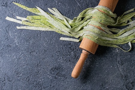 Fresh raw uncooked homemade green spinach pasta tagliatelle on wooden rolling pin over dark texture concrete background. Top view with space.の写真素材