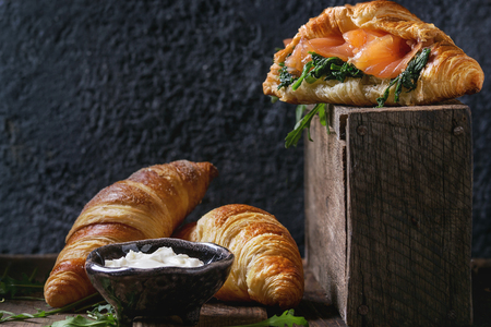 Croissant with smoked salted salmon, spinach and arugula served with bowl of cream cheese over dark old wooden table. Copy spaceの写真素材