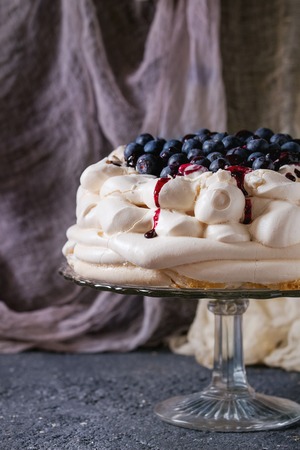 Homemade meringue cake Pavlova with whipped cream, fresh blueberries and blueberry sauce on vintage cake stand on black concrete texture background, gauze textile.の写真素材