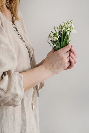 Bouquet of wild snowdrops in famale hands. Woman in white linen dress. Day light. Spring gift.の写真素材