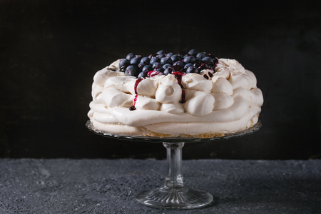 Homemade meringue cake Pavlova with whipped cream, fresh blueberries and blueberry sauce on vintage cake stand on black concrete texture backgroundの写真素材