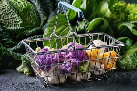 Variety of raw green vegetables salads, lettuce, bok choy, corn, broccoli, savoy cabbage, colorful young cauliflower in shop basket. Black stone texture background.の写真素材