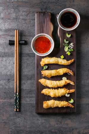 Fried tempura shrimps on lettuce salad with sauces. Served in traditional china plate with chopsticks on wood serving board and textile napkin over old metal background. Top view, space. Asian dinnerの写真素材