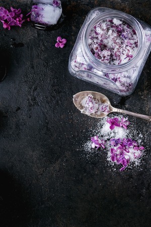 Glass jar of lilac flowers in sugar, silver spoon and ice cubes with flowers over old black iron background. Top view. Copy spaceの写真素材