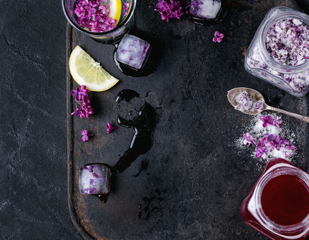 Glass of lilac water with lemon and ice cubes with flowers over old black iron background. Top view. Copy spaceの写真素材