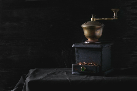 Old vintage grinder with roasted coffee beans and grind coffee in tin jar with scoop over black table with black wooden background. Dark still lifeの写真素材
