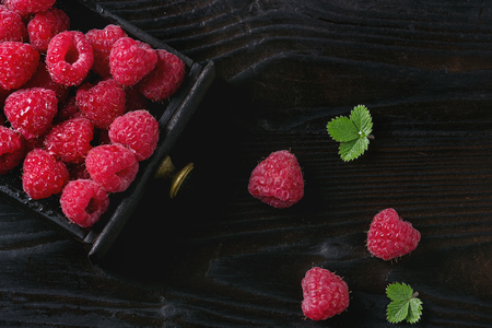 Fresh organic wet ripe raspberries in black wood box over wooden burnt background. Top view with...