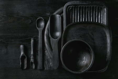 Black burnt wooden empty kitchenware cutting board, plates, scoop and spoon over black wood background. Flat lay with spaceの写真素材