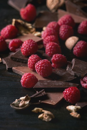 Dark and milk chopping chocolate and chips shavings chopping chocolate with fresh raspberries heap and cracks walnuts over black burnt wooden background. Close up. Chocolate dessert conceptの写真素材