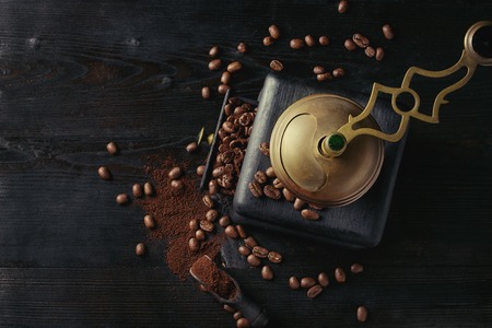 Roasted coffee beans and grind coffee in wood box with vintage coffee grinder and scoop over black wooden burnt background. Top view with space.の写真素材