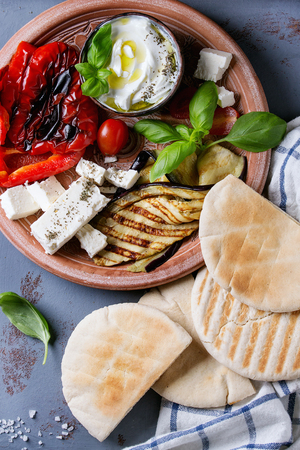 Ingredients for making pita bread sandwiches. Grilled vegetables, basil and feta cheese with flat bread on terracotta plate over gray texture background. Healthy fast food concept. Top viewの写真素材