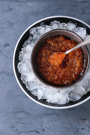 Bowl of red caviar on ice with spoon served over gray blue texture background. Top view with spaceの写真素材