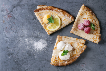 Sweet crepes pancakes with different fillings fresh raspberries, lemon curd, mascarpone cheese, mint, sugar powder over gray blue metal texture background. Top view with spaceの写真素材