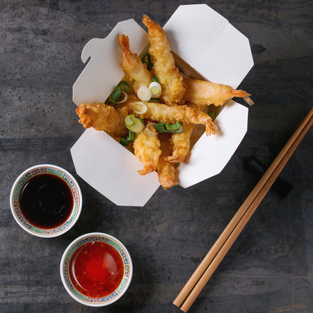 Fried tempura shrimps with rice and spring onion in paper to-go box. Served with sauces, chopsticks over old metal background. Top view, space. Asian take out dinner. Square imageの写真素材