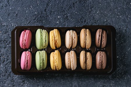 Variety of colorful french sweet dessert macaron macaroons with different fillings in balck plastic box over dark stone texture background. Top view with spaceの写真素材