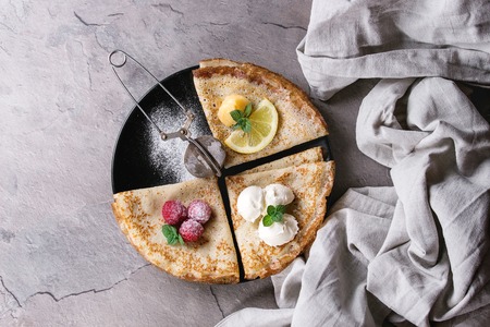 Sweet crepes pancakes with different fillings fresh raspberries, lemon curd, mascarpone cheese, mint, sugar powder with vintage sieve, textile linen over gray texture background. Top view with spaceの写真素材