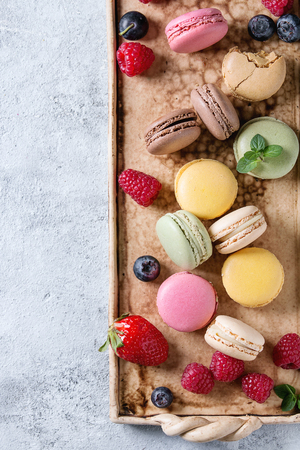 Variety of colorful french sweet dessert macaron macaroons with different fillings served on terracotta tray with fresh berries over gray texture background. Top view with spaceの写真素材