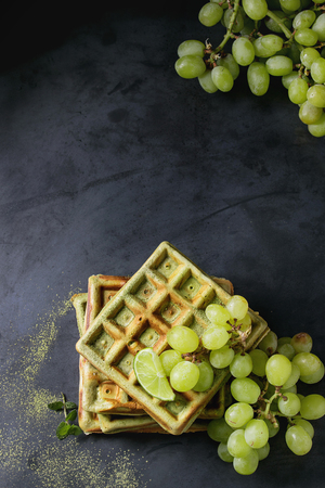 Homemade square green matcha belgian waffles with fresh ripe grapes, mint and lime over black texture metal background. Top view with spaceの写真素材