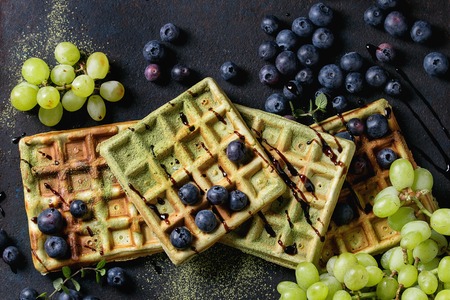 Homemade square green matcha belgian waffles with fresh ripe grapes, blueberries and mint over black texture background. Top viewの写真素材