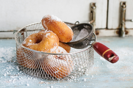 Homemade donuts with sugar powder in frying basket served with vintage sieve on blue wooden table. Rustic style, day light.の写真素材