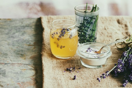 Organic raw honey, white sugar in glass jars, glass of water flavored with lavender flowers, standing on table with sackcloth. Rustic style, day lightの写真素材