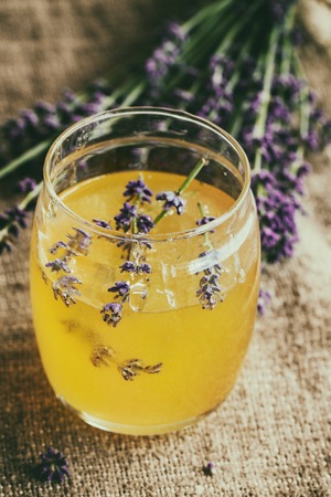 Organic raw honey in glass jar flavored with lavender flowers, standing on table with sackcloth. Rustic style, day lightの写真素材