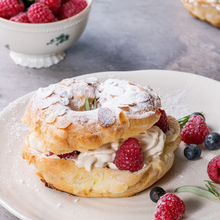 Homemade choux pastry cake Paris Brest with raspberries, almond, sugar powder, rosemary on white...