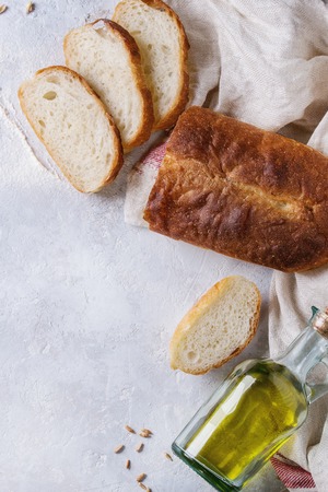 Homemade white wheat bread whole and slice served with bottle of olive oil and wheat grain seeds on white linen towel over gray texture background. Top view with space.の写真素材