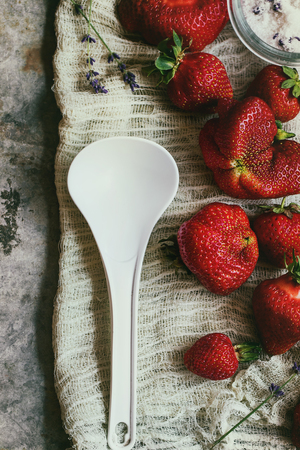 Fresh ripe strawberries prepared for making jam. Served with sugar, lavender and big white plastic spoon on gauze over gray metal background. Preserving concept. Top view. Rustic style, day lightの写真素材