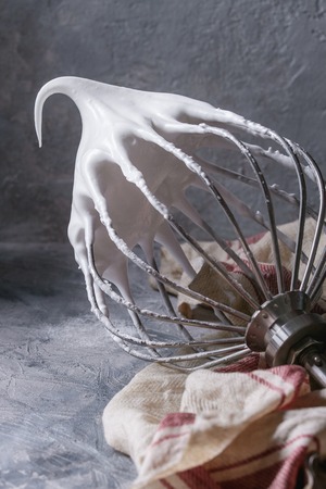 Process of cooking meringue. Whipped egg whites on mixer whisk on linen towel over gray texture...