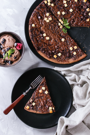 Dessert chocolate pizza with dark, milk, white chocolate, served on black plate with fork, mint, frozen berries and bowl of ice cream over gray concrete background with textile linen. Top viewの写真素材