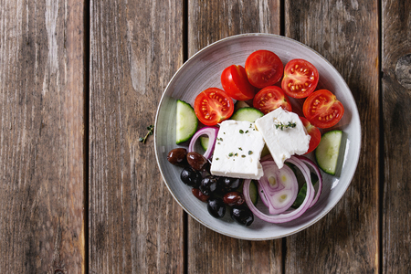Ingredients for traditional greek salad. Cherry tomatoes, sliced cucumbers, red onion, black olives, feta cheese gray ceramic plate over wooden plank background. Top view with copy spaceの写真素材