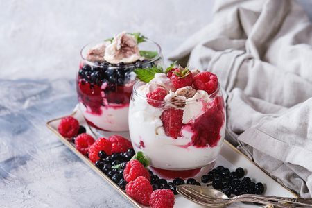 Traditional summer dessert Eton Mess. Broken meringue with whipped cream, berry jam, fresh blueberries and raspberries in two glasses, decorated with mint leaves over gray concrete background.