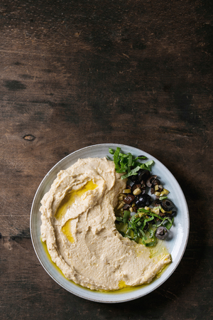 Homemade traditional spread hummus with chopping olives and herbs on blue plate, served over old wooden background. Mediterranean snack. Flat lay, copy spaceの写真素材