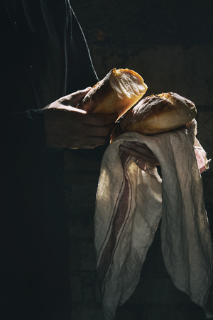 Loaf of fresh baked wheat bread in man's hands in sunshine. Rustic day light in dark room. Toned imageの写真素材