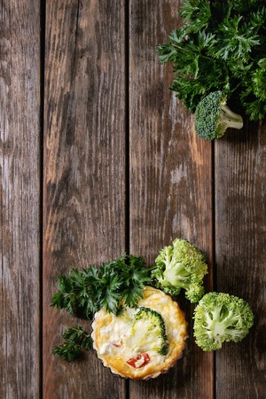 Baked homemade quiche pie in mini metal forms served with fresh greens on old plank wooden background. Flat lay with spaceの写真素材