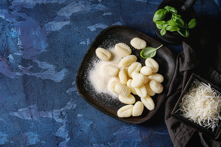 Raw uncooked potato gnocchi in black wooden plates with ingredients. Flour, grated parmesan cheese, basil, over dark blue concrete background. Top view. Home cooking.の写真素材