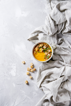 Bowl of vegetarian pumpkin carrot soup served with croutons and onion on textile linen over gray concrete background. Top view with copy spaceの写真素材