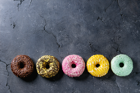 Variety of colorful glazed donuts over black texture background. Top view with spaceの写真素材