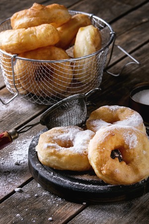 Homemade donuts with sugar powder on black serving board and in frying basket served with vintage...