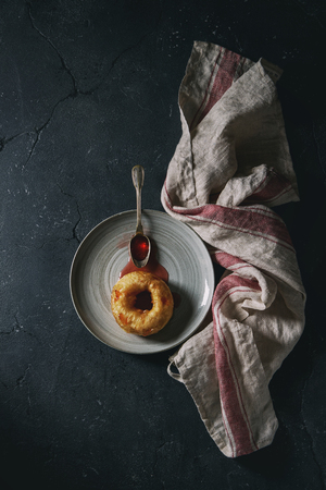 Homemade donut with jam on gray plate with vintage spoon and textile towel over dark texture background. Top view with spaceの写真素材