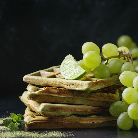 Homemade square green matcha belgian waffles with fresh ripe grapes, mint and lime over black metal background. Close up with space. Square imageの写真素材