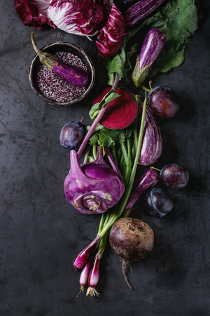 Assortment raw organic of purple vegetables mini eggplants, spring onion, beetroot, radicchio salad, plums, kohlrabi, flower salt over dark metal background. Top view with spaceの写真素材