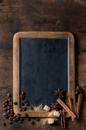 Empty vintage chalkboard, coffee beans, spices, brown sugar over old wooden background. Top view with space for text.の写真素材
